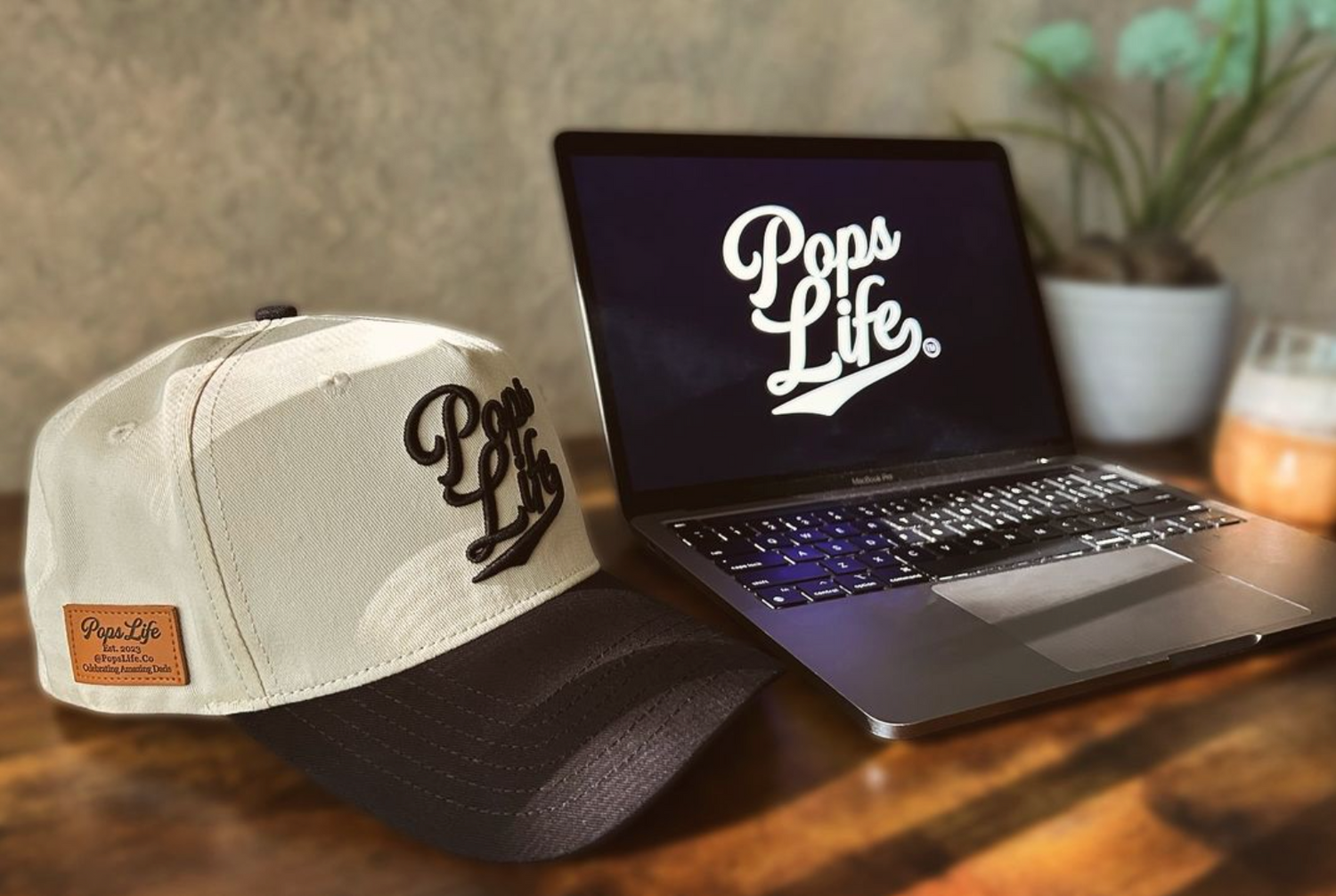 Best Dad Hats by PopsLife: A stylish PopsLife dad hat in beige and black displayed next to a laptop with the PopsLife logo, perfect for dads who value quality and design.