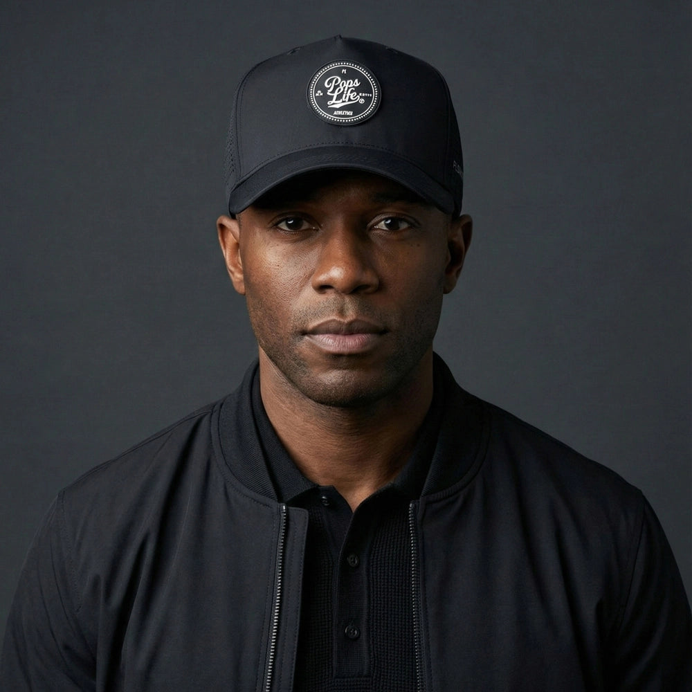 Man wearing a Pops Life Athletic Black Dad Hat and jacket against a dark background
