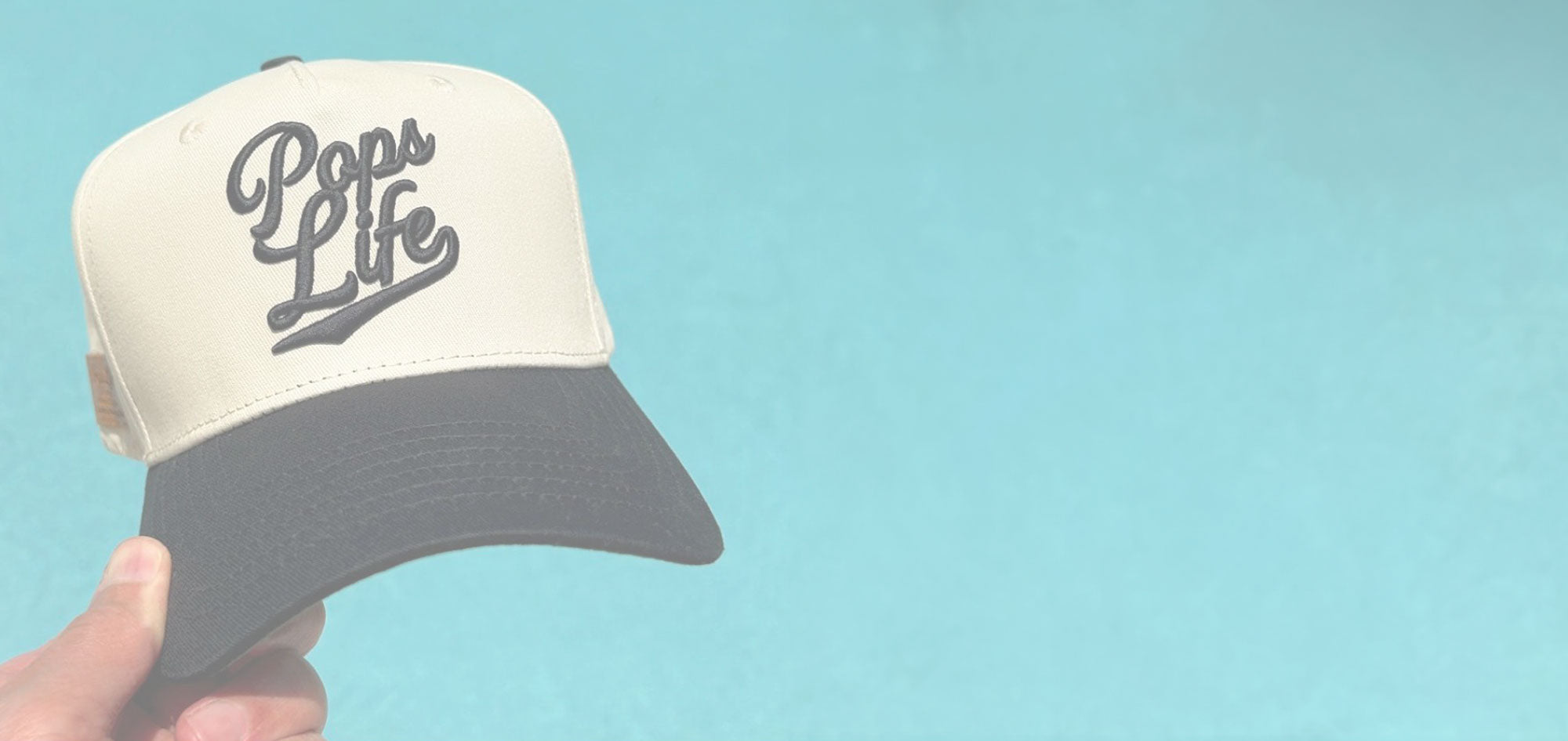 Close-up of a designer dad hat with Pops Life logo on a turquoise background.