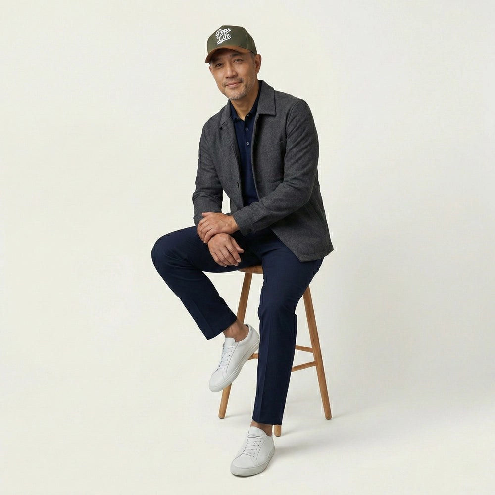 Man sitting on a stool wearing a gray blazer, navy pants, white sneakers, and a Pops Life Hunter Green Dad Hat.