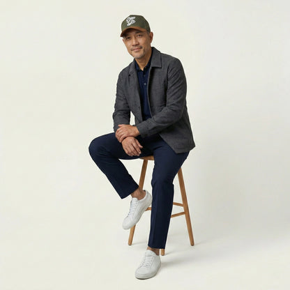 Man sitting on a stool wearing a gray blazer, navy pants, white sneakers, and a Pops Life Hunter Green Dad Hat.