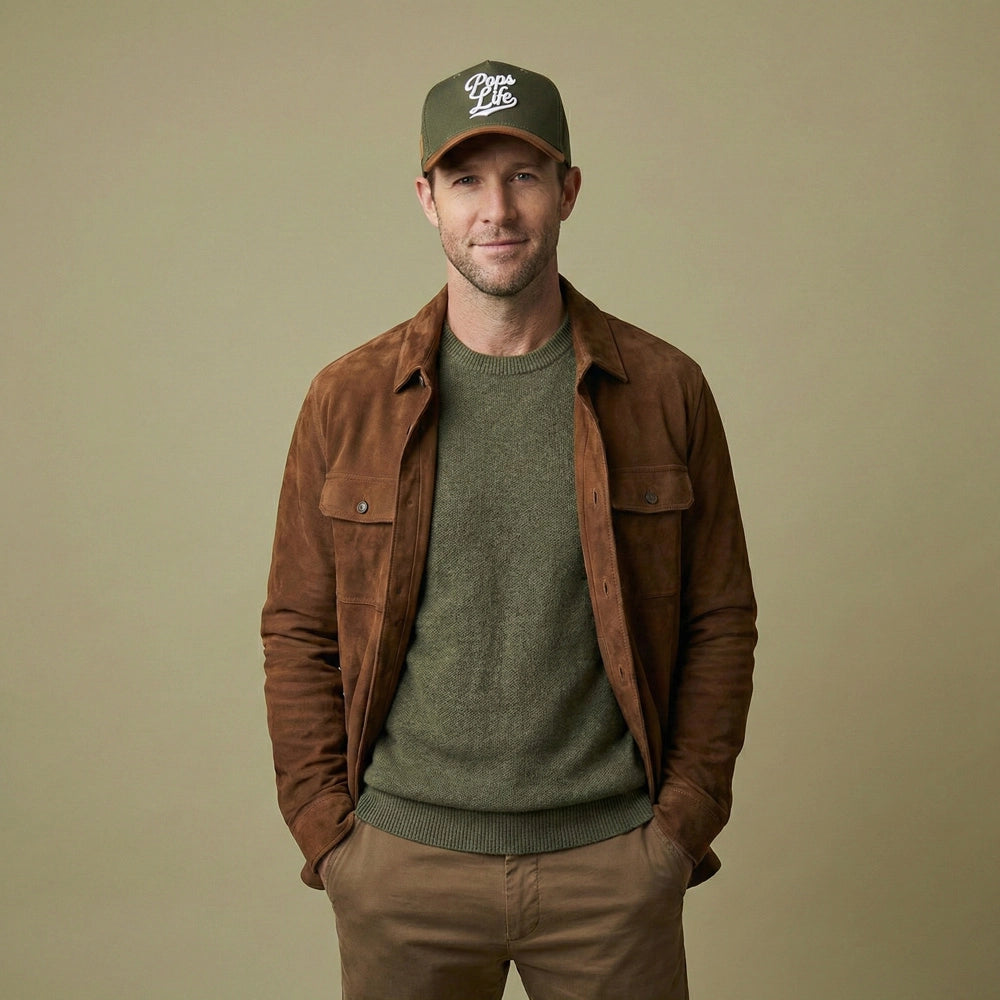 Man wearing a brown jacket, green sweater, and Pops Life Hunter Green Dad Hat on a beige background