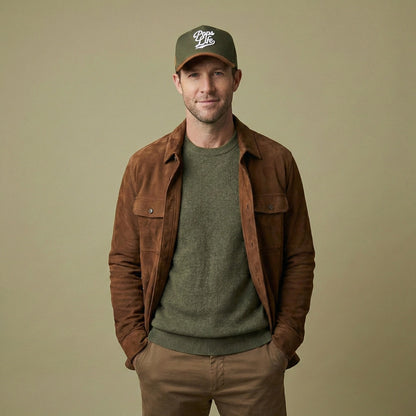 Man wearing a brown jacket, green sweater, and Pops Life Hunter Green Dad Hat on a beige background