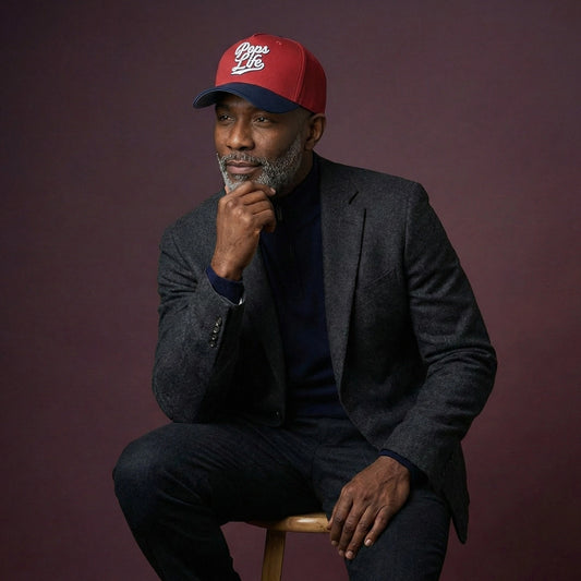 Man wearing a Pops Life Maroon and Navy Dad Hat, sitting on a stool against a purple background