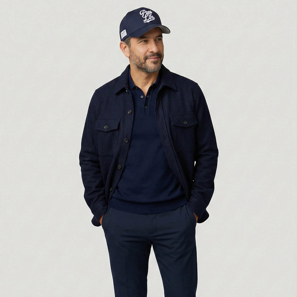 Man wearing a navy jacket, shirt, and Pops Life Navy blue Dad Hat on a light gray background